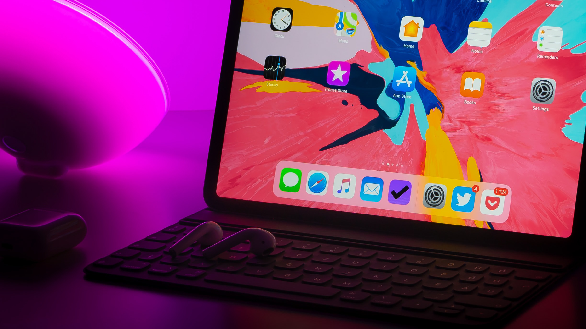 ipad pro keyboard and earbuds in pink background